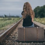 Portrait of young sad ten girl standing with suitcase outdoors a